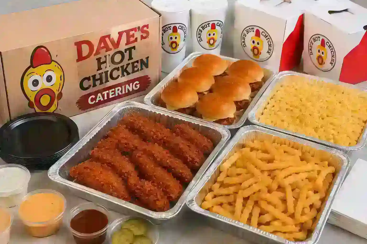 Dave’s Hot Chicken catering spread with chicken tenders, sliders, fries, mac and cheese, sauces, and drinks